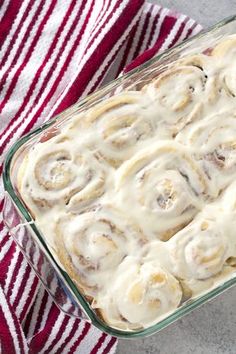 a glass dish filled with cinnamon rolls on top of a red and white striped towel