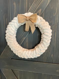 a white rope wreath with a bow hanging on a wooden door