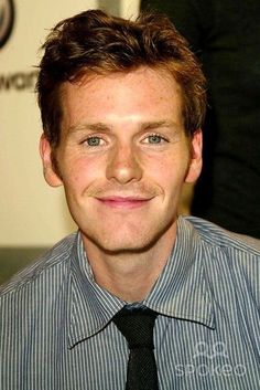 a man wearing a striped shirt and tie smiling at the camera with his eyes wide open