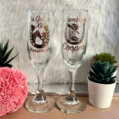 two wine glasses sitting on top of a table next to a potted plant and pink flower