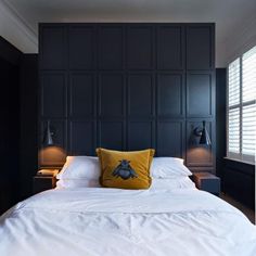 a bedroom with black walls and white bedding, two lamps on either side of the bed