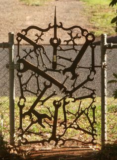 an iron sculpture in the shape of a clock on a chain link fence near a grassy area