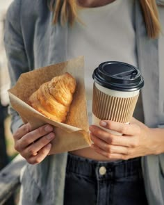 a woman holding a cup of coffee and a croissant wrapped in paper with both hands