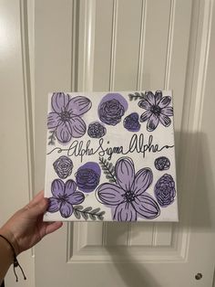 a hand holding up a purple and white sign with flowers on it that says, aloha & samna aloha