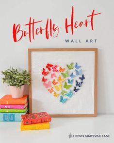 the butterfly heart wall art is next to books and a potted plant on a table