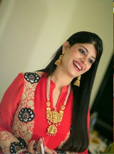 a woman with long black hair wearing a red top and gold jewelry smiling at the camera