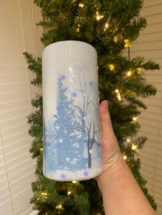 a hand holding up a frosted cup with trees on it and snow flakes