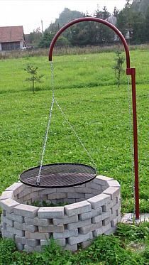 an outdoor fire pit in the middle of a grassy field with a red pole and water spout