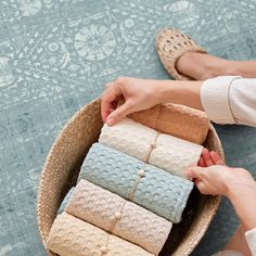 a woman is holding several folded towels in a basket on the floor next to her feet