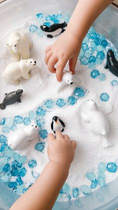 a child is playing with penguins and polar bears in an ice play tray filled with water