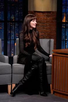 a woman sitting on top of a gray couch in front of a tv screen wearing black boots