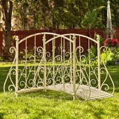 a white wrought iron bed frame sitting in the middle of a yard with green grass