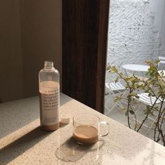 a bottle of liquid sitting on top of a counter next to a cup and saucer