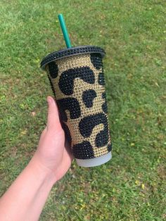 a hand holding a cup with a straw in it on top of green grass next to a field