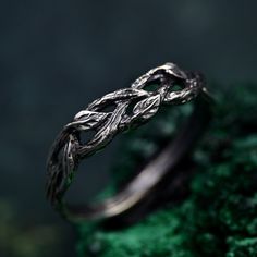 a silver ring sitting on top of a green mossy surface with leaves in the middle