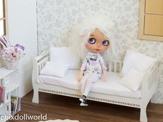 a doll sitting on a white bench in a room with floral wallpaper and pillows