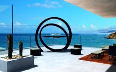 an artistic view of the ocean from a modern house overlooking the beach with lounge chairs and cacti