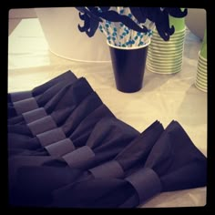 there are many folded black cloths next to each other on the table with cups in the background