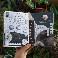 a hand holding an open notebook with drawings on it and the moon in the sky