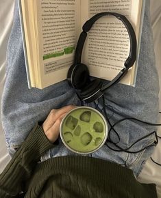 a person with headphones is reading a book and holding a bowl of green liquid