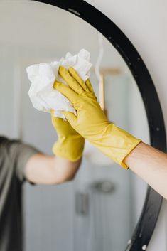 a person in yellow gloves wiping up a mirror with a cloth on top of it