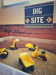 toy construction vehicles sitting on top of a pile of sand next to a sign that says dig site