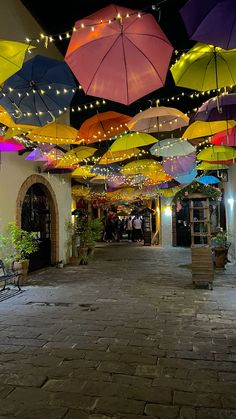 many colorful umbrellas hanging from the ceiling in an open area with tables and chairs