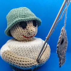 a crocheted doll with a green hat holding a knitting needle and an umbrella