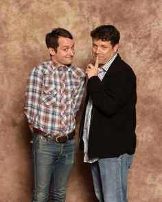 two men standing next to each other in front of a wall