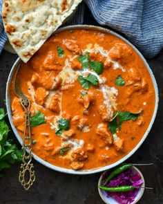 a bowl filled with red curry next to pita bread and garnished with cilantro