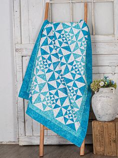 a blue and white quilt sitting on top of a wooden chair next to a potted plant