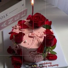 a pink cake with red roses on it and a single candle in the middle that is lit