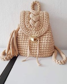 a straw bag with tassels on the front and side, sitting against a white wall