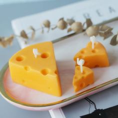 two slices of cheese on a plate with some candles in the shape of trees and leaves