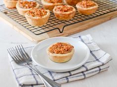 a white plate topped with mini pies next to a cooling rack filled with cupcakes