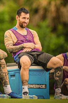 a man sitting on top of a blue box next to another man in purple shirt