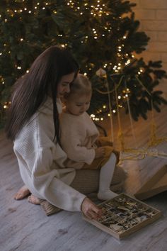 a woman sitting on the floor next to a christmas tree holding a baby in her lap