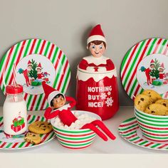 an elf is sitting in a bowl with cookies and milk on the table next to it