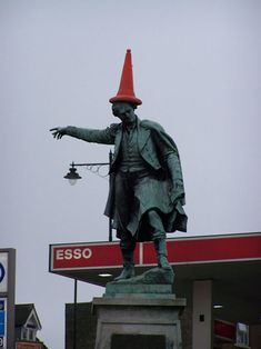 there is a statue with a red hat on it's head and a gas station sign in the background