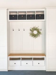 an entryway with white cabinets and drawers, a wreath on the wall above it