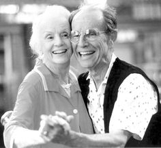 an older couple is dancing together in the street with their arms around each other and smiling