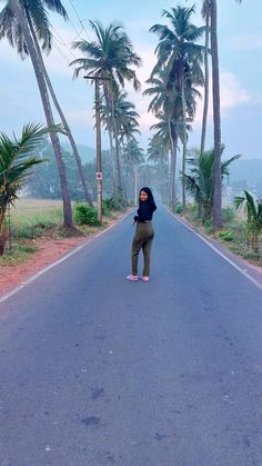 a woman standing on the side of an empty road with palm trees in the background