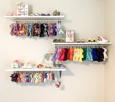 two white shelves filled with baby clothes and shoes next to a wall mounted book shelf