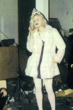 an old photo of a woman in a fur coat talking on a cell phone while standing next to other people