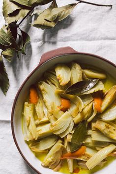 a pot filled with vegetables sitting on top of a white table cloth next to a leafy branch