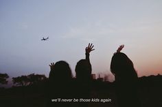 two girls are reaching up to the sky with their hands in the air and an airplane flying overhead