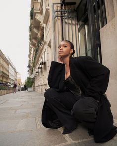 a woman is sitting on the ground in front of a building and looking off into the distance