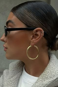 a woman wearing large gold hoop earrings and a white sweater is looking away from the camera