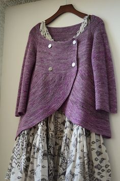 a purple cardigan is hanging on a wall next to a white and black dress