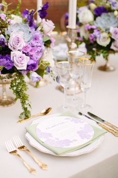 the table is set with purple and white flowers, silverware, and gold place settings